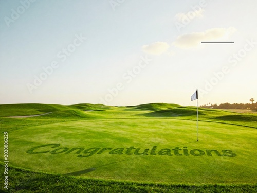 Golf Elegant luxury golf course scene featuring the word “Congratulations” cut neatly into the grass on a pristine putting green beside the hole and flag. Soft golden sunlight