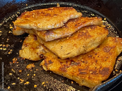 Vegan seitan schnitzel slices frying in cast iron pan, cut steak style