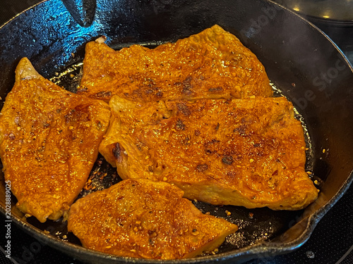 Vegan seitan schnitzel slices frying in cast iron pan, cut steak style