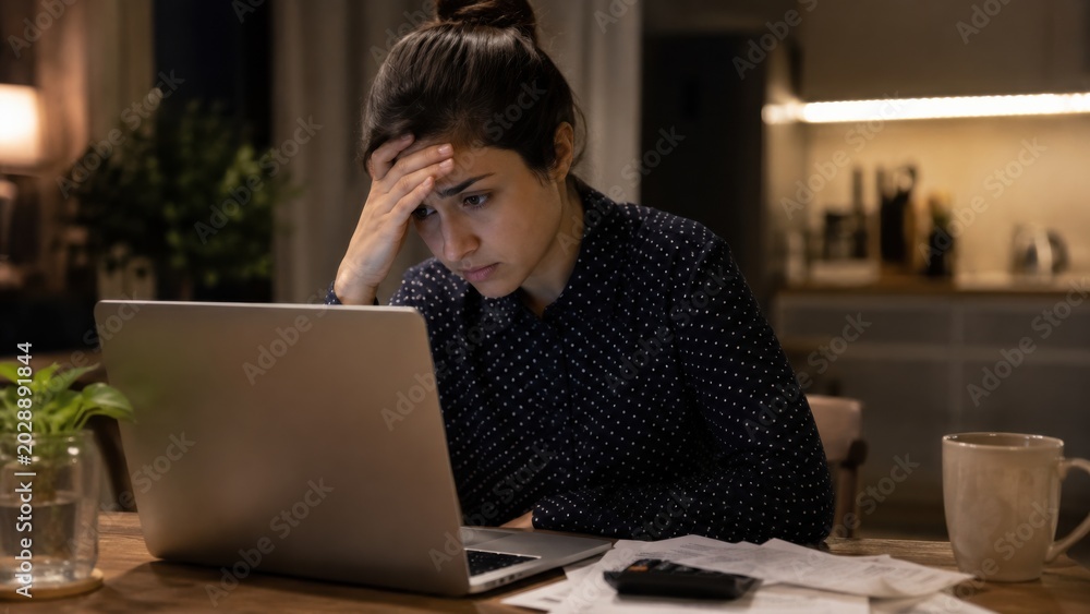 Fototapeta premium Frustrated young professional working late at home office with laptop and coffee