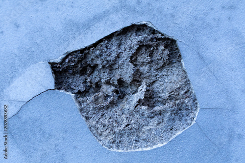 Close up of a damaged concrete wall with a large hole revealing broken cement layer.