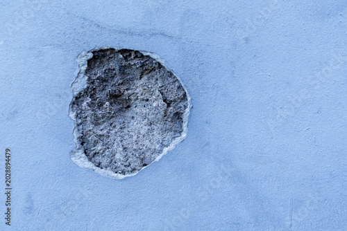 Close up of a damaged concrete wall with a large hole revealing broken cement layer.