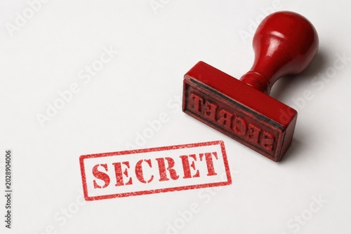 Red rubber stamp with SECRET text on white paper confidentiality concept minimalist flat lay