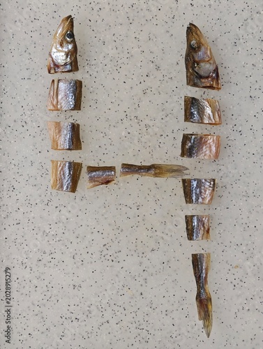 Close-up top-down view of appetizing pieces of dried vobla fish, carefully cut and creatively arranged to form the numeral 4, laid out on a light speckled kitchen countertop, symbolizing a savory