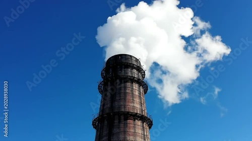 Industrial smokestack emitting billowing white smoke against a vibrant blue sky on a sunny day