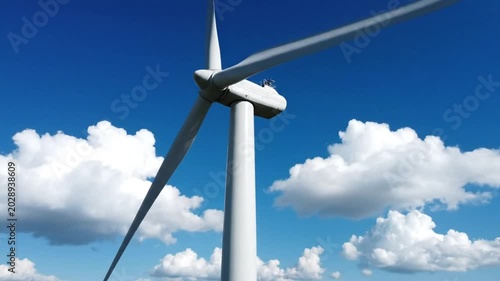 Low angle view of wind turbine blades rotating in bright sunshine with fluffy clouds