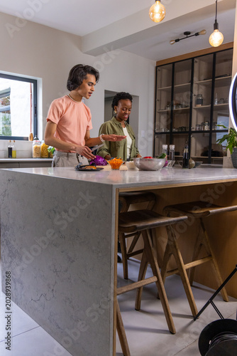 Diverse couple preparing salad on marble kitchen island with bowls of cabbage and carrots