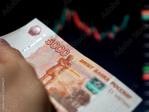 Cash in Hand with Russian 5000 Ruble Bill and Stock Chart