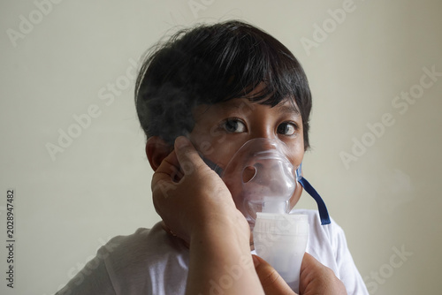 Tableau sur toile Close up young child receiving respiratory treatment, person hand helping to wearing mask, focus on eyes glance and unwell face expression
