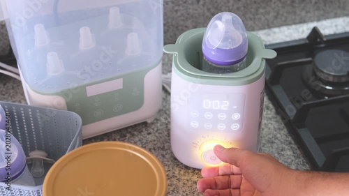 Parent preparing and heating infant milk in an electric warmer on the kitchen counter