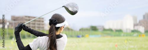 打ちっぱなしのゴルフ練習場でドライバーショットをスウィングする若い女性のゴルファーのスポーツイメージ　顔無しの後ろ姿バナー