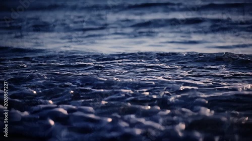 A dark, moody ocean wave crashes with foamy white crests under a shadowy sky