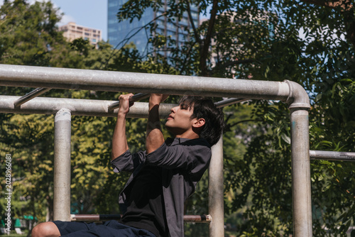 Photography Young Asian man performing pull-ups for upper body strength on outdoor monkey bars in a park