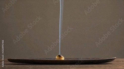 Raw frankincense resin burning on dark wood, thin gray smoke rising.