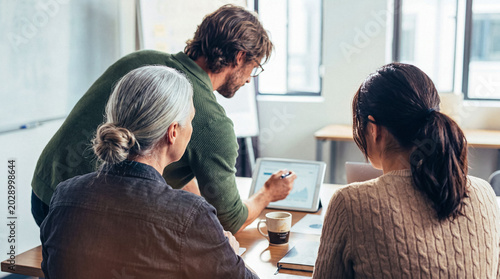 Photos Collaborative business team discussing financial data and project plans on a digital tablet in a modern meeting room