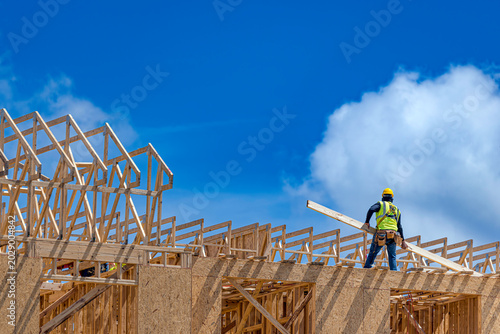 Quadro su tela Construction worker standing on the top plate of a wooden house frame and carryi
