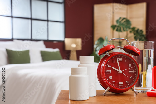 Tableau sur toile Red alarm clock with pills and glass of water on table in bedroom