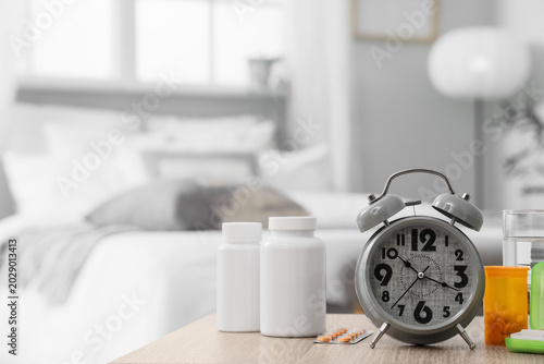 Tableau sur toile Alarm clock with pills and glass of water on table in bedroom