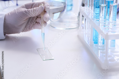 Female scientist's hand dropping water sample onto glass on table in laborato...