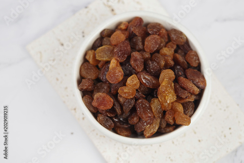 Fotografía A bowl holds raisins on a plain surface