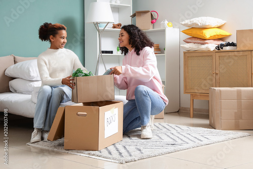 Happy African-American woman and her daughter packing things into cardboard b...