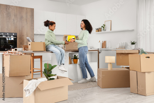 Happy African-American woman and her daughter packing toaster into cardboard ...