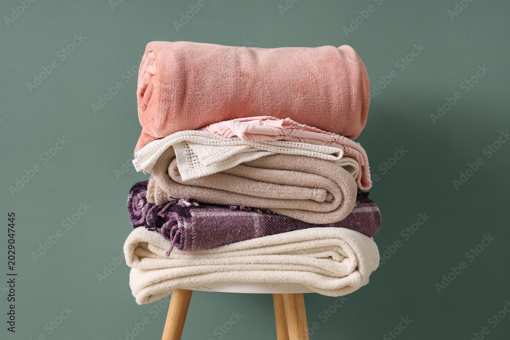 Naklejka premium Stack of different cozy blankets on chair against turquoise background