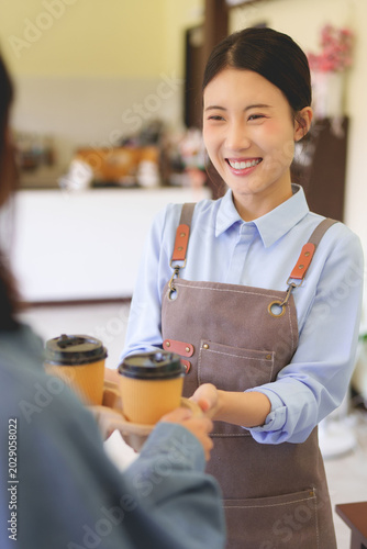Asian barista woman serving coffee to customer at cafe counter wearing apron smiling friendly service hospitality small business owner working at coffee shop