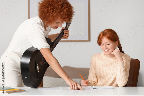 Young happy woman with notes giving acoustic guitar lessons to teenage girl a...