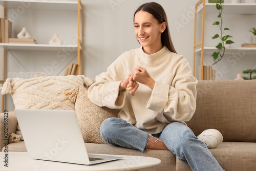 Young happy woman video chatting in sign language on sofa at home