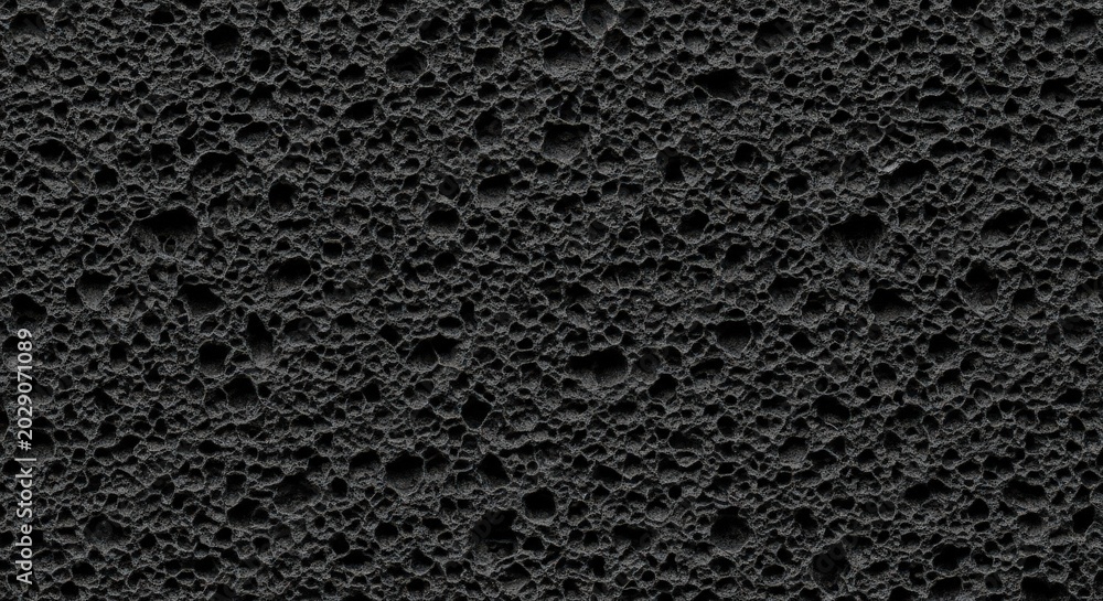 Fototapeta premium Textured black porous volcanic rock surface with rough pits and deep shadows Wallpaper Background image
