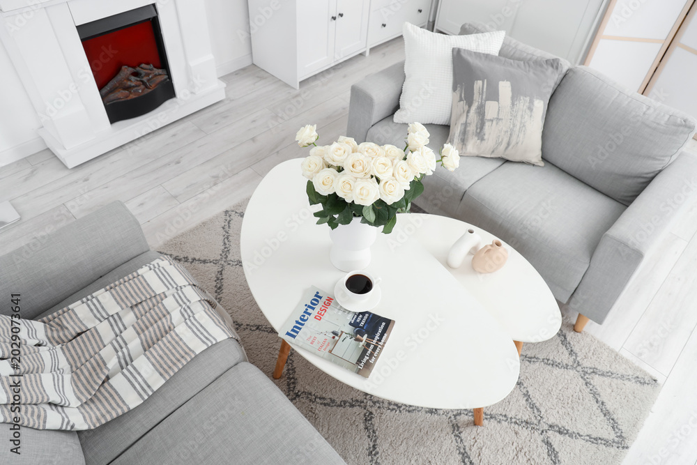 Fototapeta premium Interior of light living room with sofas, tables and white roses in vase, top view