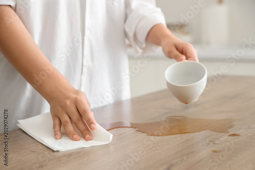 Konstfotografi Woman wiping spilled coffee with paper towel on table in kitchen, closeup