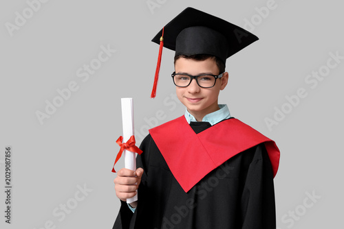 Schoolboy in bachelor robe with diploma on grey background
