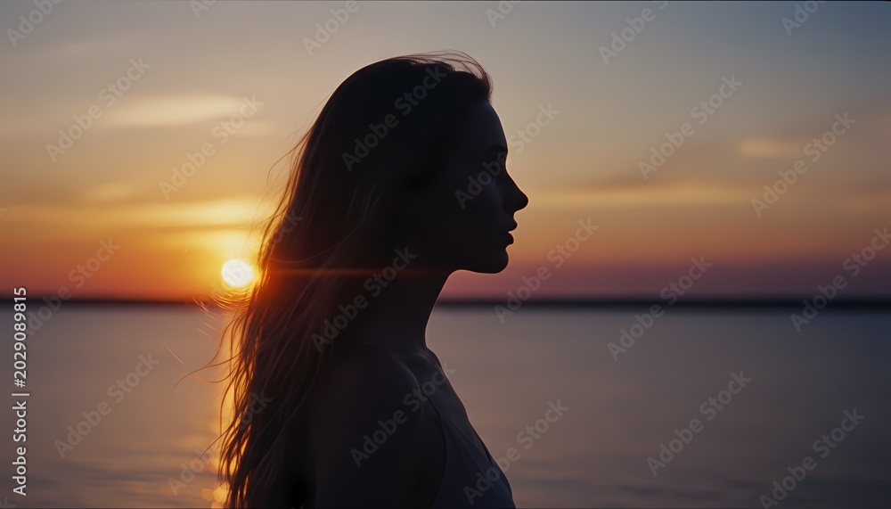 Fototapeta premium 海辺の美しい夕日を見つめる女性の横顔のシルエット、シネマティック