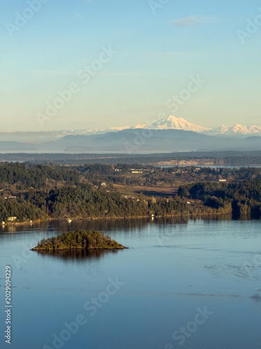 A small island in a tranquil bay and snow capped mountains in the distance