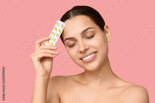 Pretty young woman holding blister pack of vitamin A capsules on pink background