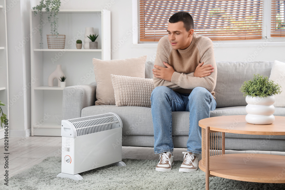 Obraz premium Frozen young man warming near radiator at home