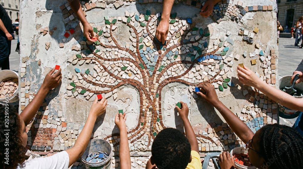 Fototapeta premium A group of people creating a mosaic art piece with a tree design on a sunny day outdoors