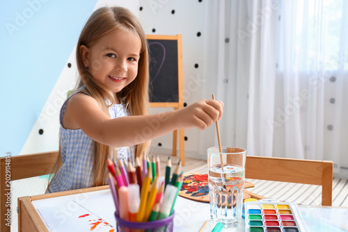 Cute little girl drawing with paints at home