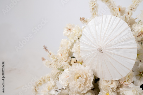 Detail with white japanese vibe umbrela, Elegant white flowers cascade upward in graceful tiers. Delicate blooms and soft petals frame a clean, minimalist backdrop. Neutral tones enhance purity