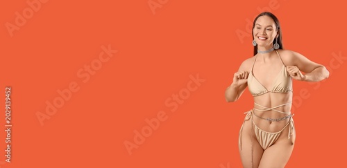 Bild auf Leinwand Beautiful woman in stylish beige swimsuit and with jewellery on orange backgroun