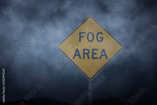 Fotografie A yellow diamond shaped traffic sign stating Fog Area in dense fog