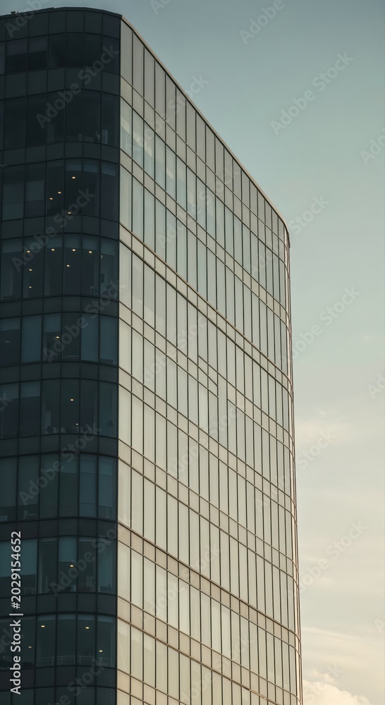 Fototapeta premium Modern Glass Skyscraper: A contemporary glass office building stands tall against a serene sky, its sleek facade reflecting the soft light of dawn, symbolizing progress and urban development.