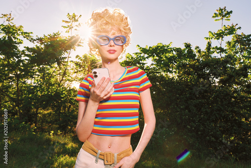 Bild auf Leinwand Young woman with curly blonde hair and blue sunglasses wears a colorful striped