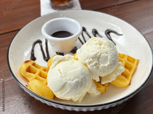 close up photo of waffle with ice cream and chocolate paste topping on a white plate