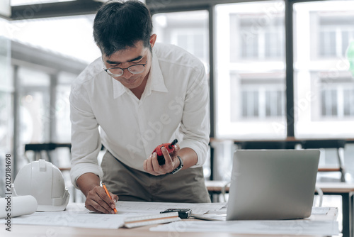 Young Man in White Shirt Analyzing Construction Blueprint in Modern Office