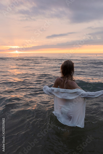 silhouette of a beautiful girl in a shirt standing by the sea against the sunset
