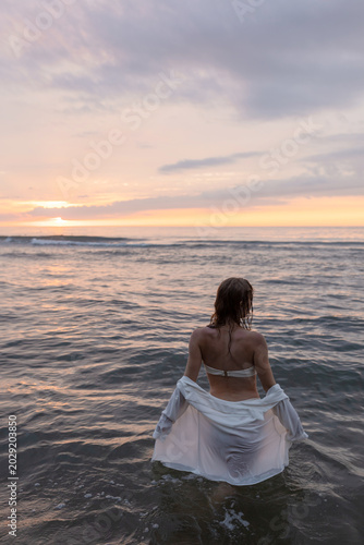 silhouette of a beautiful girl in a shirt standing by the sea against the sunset
