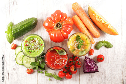 Top view of assorted fresh cold vegetable soups and raw ingredients on white wooden table